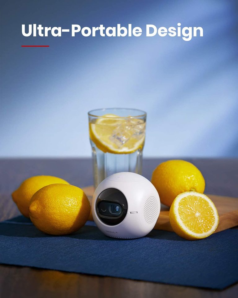 A Nebula Astro portable projector sits next to a group of lemons with a glass of lemon water set up behind them.