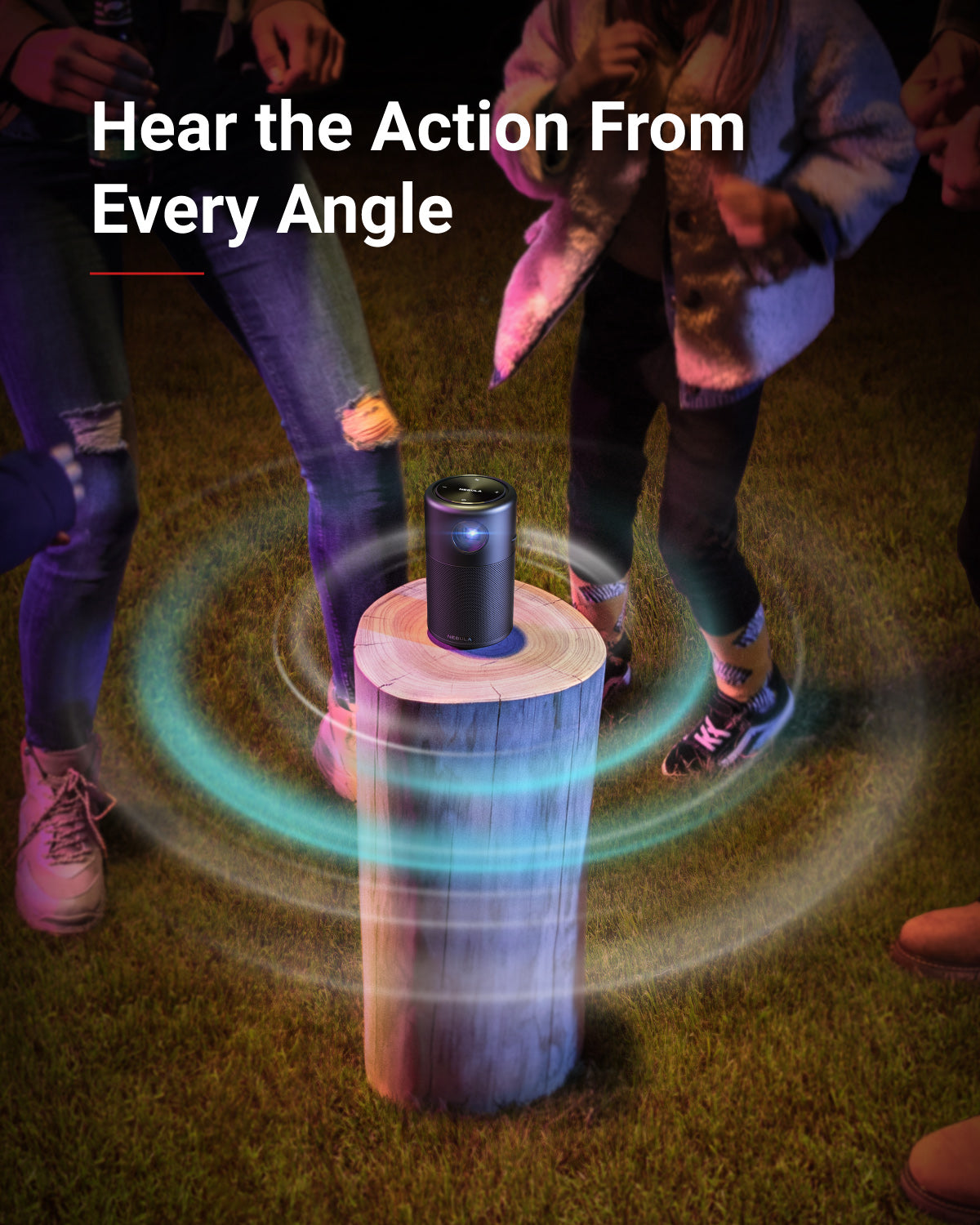 People dance around a Nebula Capsule portable projector, which sits on top of a log and has swirls emanating from it.
