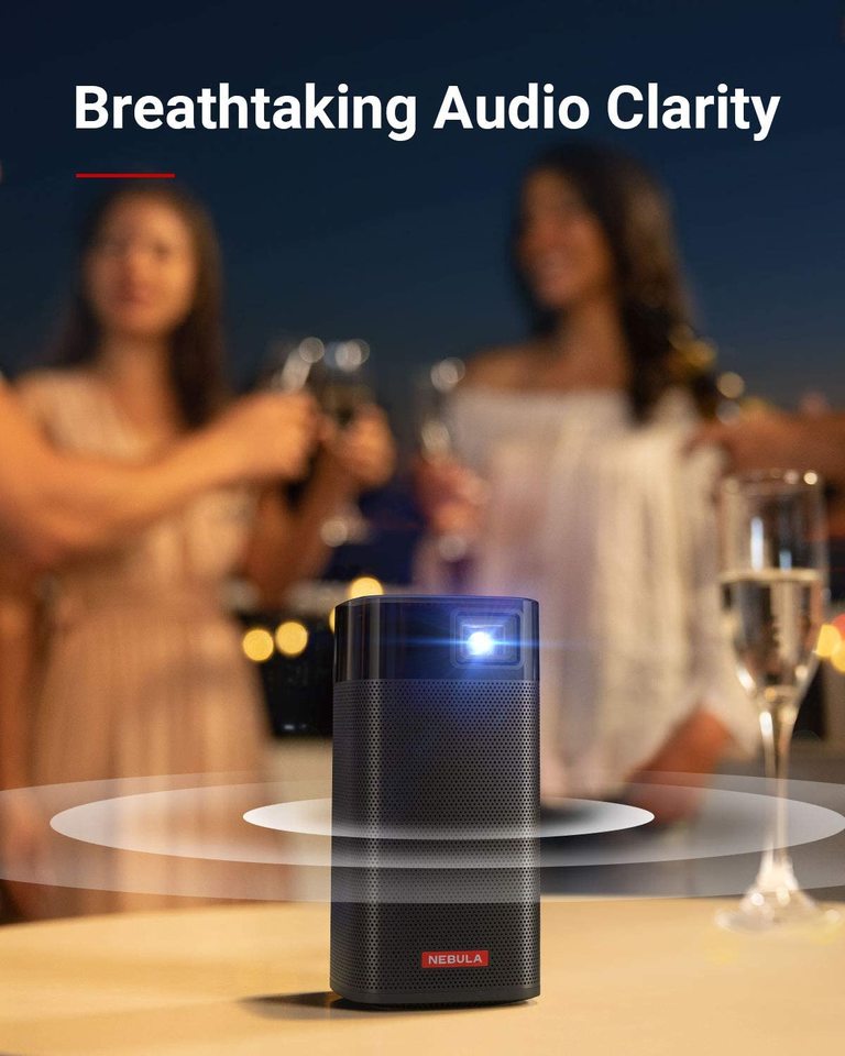 An Apollo portable projector sits on a table with a glass of wine while emanating waves of audio to two women behind it.